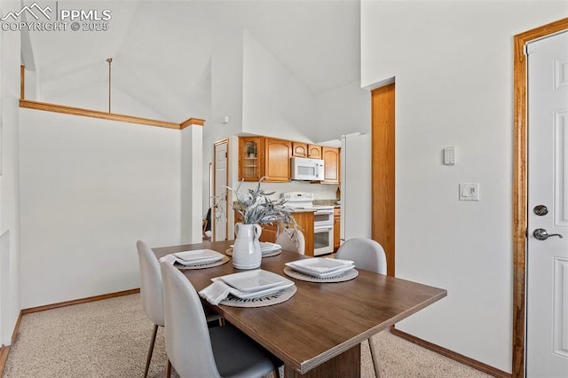 dining space featuring high vaulted ceiling, light colored carpet, and baseboards