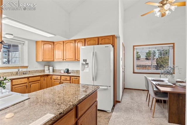 kitchen with white fridge with ice dispenser, light stone counters, plenty of natural light, and high vaulted ceiling