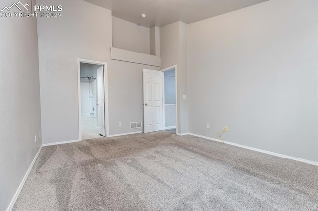 unfurnished bedroom with baseboards, visible vents, connected bathroom, a high ceiling, and carpet floors