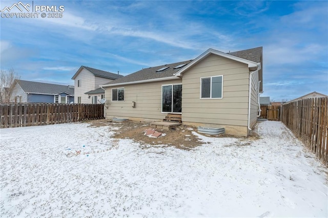 snow covered house featuring entry steps and a fenced backyard