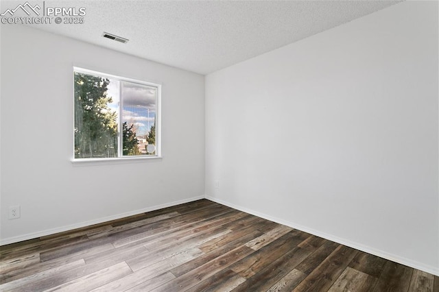 empty room featuring dark wood-style flooring, visible vents, a textured ceiling, and baseboards