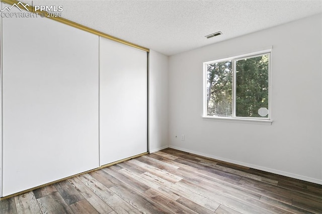 unfurnished bedroom with a closet, visible vents, a textured ceiling, wood finished floors, and baseboards