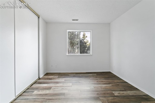 unfurnished bedroom with visible vents, a textured ceiling, baseboards, and wood finished floors