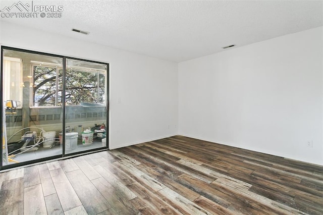 spare room featuring a textured ceiling, visible vents, and wood finished floors