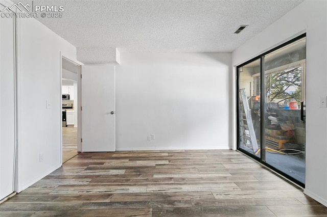 unfurnished room featuring a textured ceiling, wood finished floors, visible vents, and baseboards