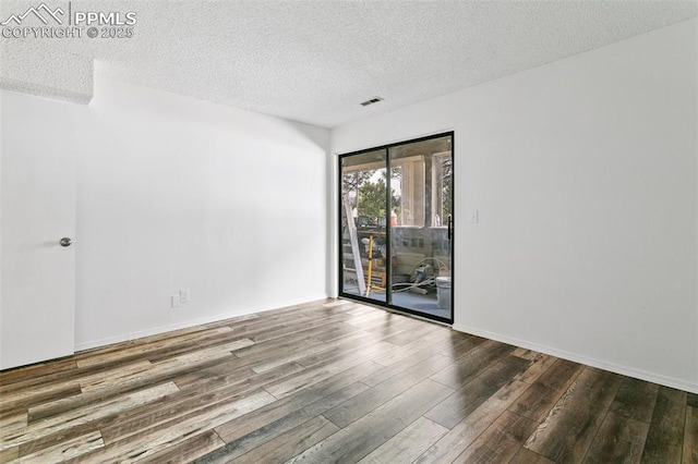 unfurnished room with a textured ceiling, wood finished floors, visible vents, and baseboards