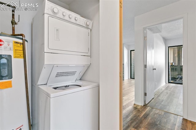 washroom featuring laundry area, wood finished floors, a textured ceiling, stacked washing maching and dryer, and water heater