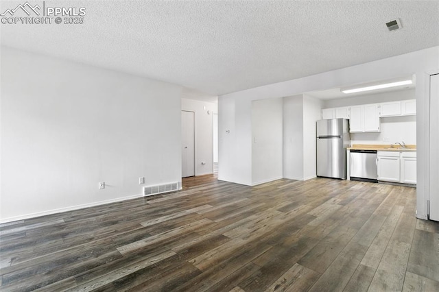 unfurnished living room with a sink, a textured ceiling, dark wood finished floors, and visible vents