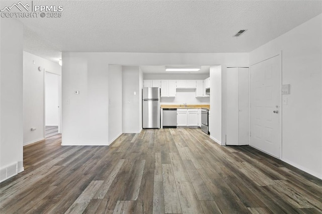 unfurnished living room with visible vents, dark wood finished floors, and a textured ceiling