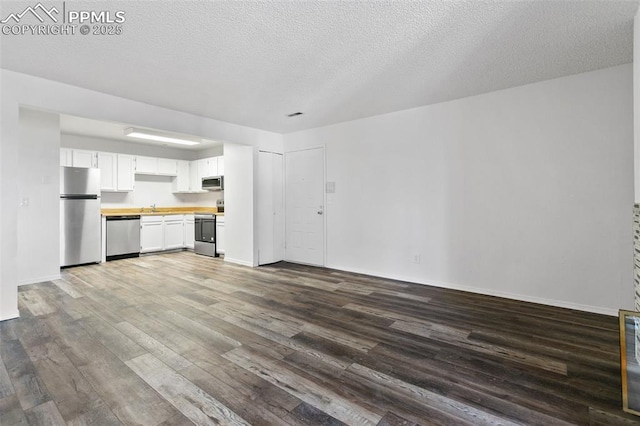 interior space with wood finished floors, stainless steel appliances, a textured ceiling, light countertops, and white cabinetry