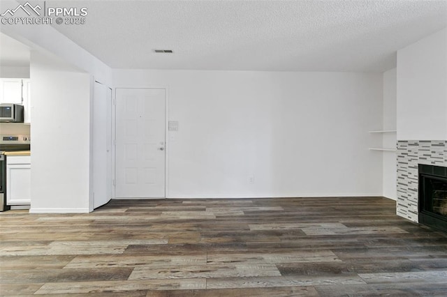 unfurnished living room with a textured ceiling, visible vents, a tiled fireplace, and wood finished floors