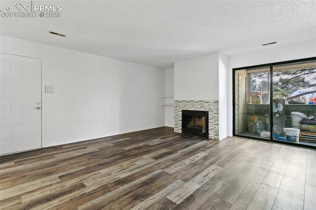 unfurnished living room featuring visible vents, a textured ceiling, a tiled fireplace, and wood finished floors