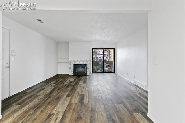 unfurnished living room featuring dark wood-style flooring, visible vents, a textured ceiling, a tile fireplace, and baseboards