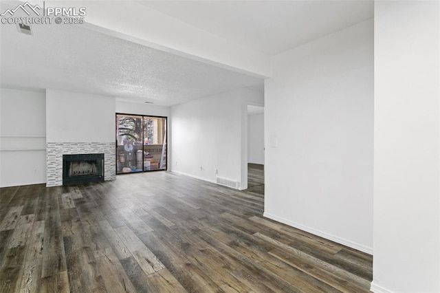 unfurnished living room with a textured ceiling, a tile fireplace, dark wood-type flooring, visible vents, and baseboards