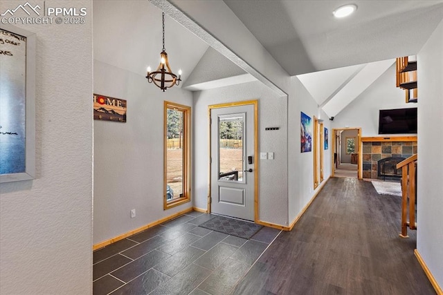 foyer entrance with baseboards, a tiled fireplace, lofted ceiling, dark wood-type flooring, and a notable chandelier