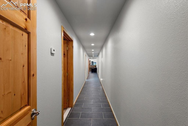 hallway with recessed lighting, dark tile patterned floors, baseboards, and a textured wall