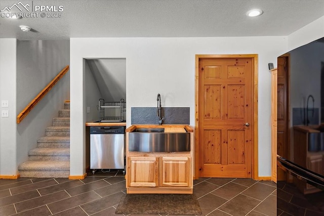 kitchen featuring freestanding refrigerator, a sink, a textured ceiling, dishwasher, and baseboards