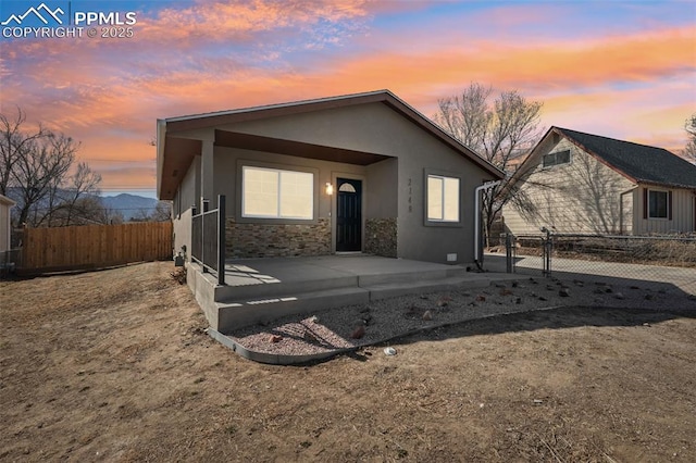 view of front of property featuring stucco siding, a gate, a patio area, fence, and stone siding