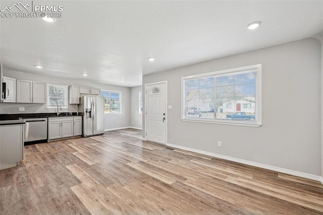 kitchen with stainless steel appliances, dark countertops, light wood-style floors, a sink, and baseboards