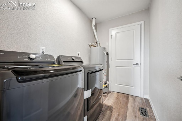 clothes washing area with washing machine and dryer, laundry area, wood finished floors, baseboards, and water heater