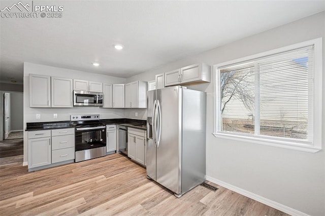 kitchen featuring appliances with stainless steel finishes, dark countertops, visible vents, and light wood-style floors