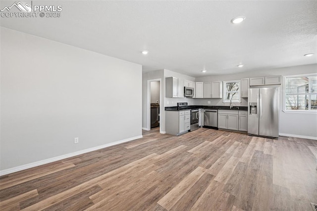 kitchen featuring baseboards, light wood-style floors, appliances with stainless steel finishes, washer / clothes dryer, and dark countertops