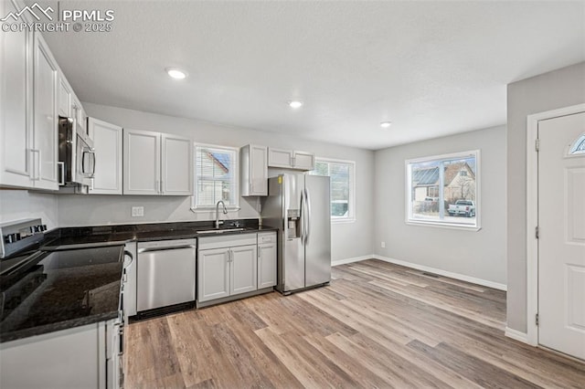 kitchen with light wood finished floors, baseboards, stainless steel appliances, a sink, and recessed lighting