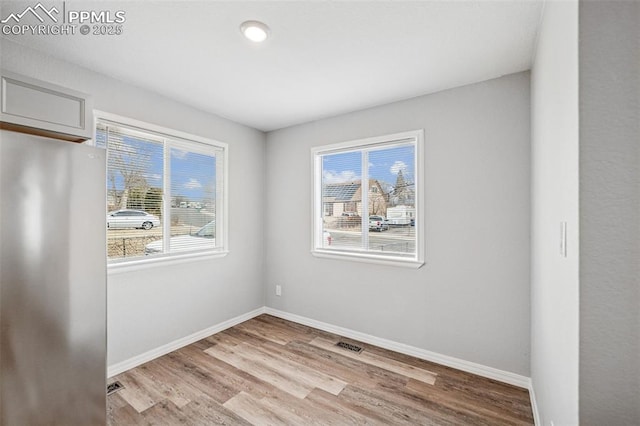 spare room with light wood-style floors, a healthy amount of sunlight, and baseboards