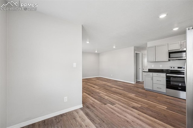 kitchen featuring stainless steel appliances, dark countertops, wood finished floors, and baseboards