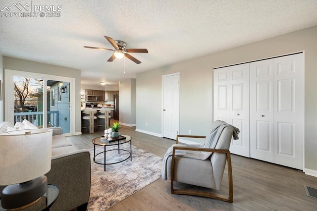 living area featuring dark wood-style floors, ceiling fan, a textured ceiling, and baseboards