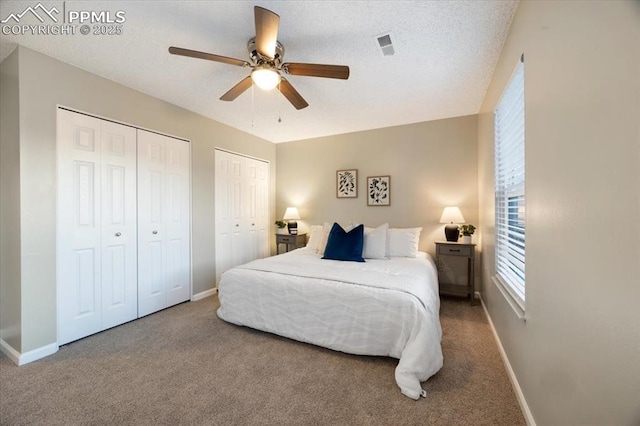 carpeted bedroom featuring ceiling fan, a textured ceiling, baseboards, and two closets