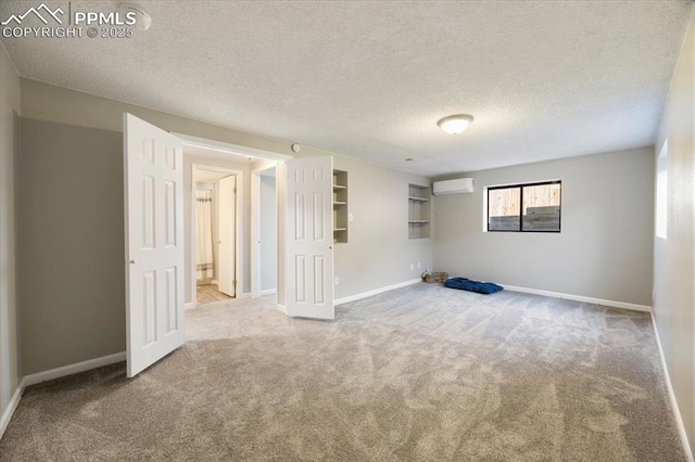 carpeted spare room featuring a textured ceiling, a wall mounted AC, and baseboards