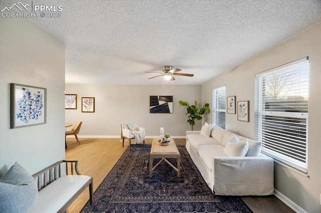 living area featuring ceiling fan, a textured ceiling, baseboards, and wood finished floors