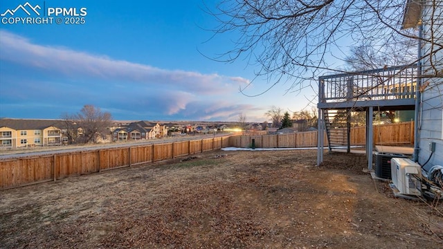 yard at dusk featuring stairs, central AC, and a fenced backyard