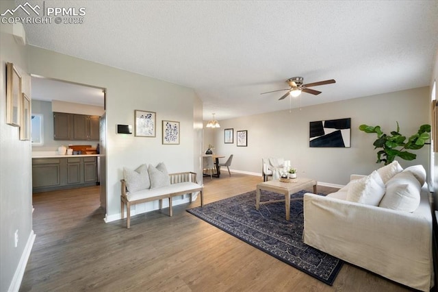 living area with a textured ceiling, baseboards, wood finished floors, and ceiling fan with notable chandelier