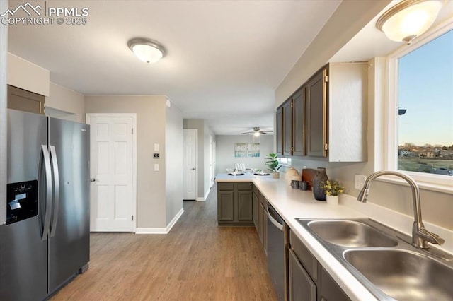 kitchen featuring light countertops, light wood-style flooring, appliances with stainless steel finishes, a sink, and baseboards