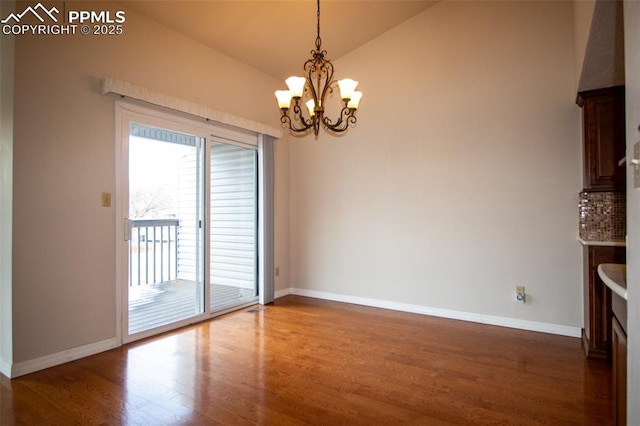 unfurnished dining area featuring lofted ceiling, a notable chandelier, baseboards, and wood finished floors