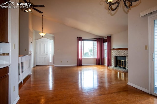 unfurnished living room featuring a brick fireplace, vaulted ceiling, baseboards, and wood finished floors