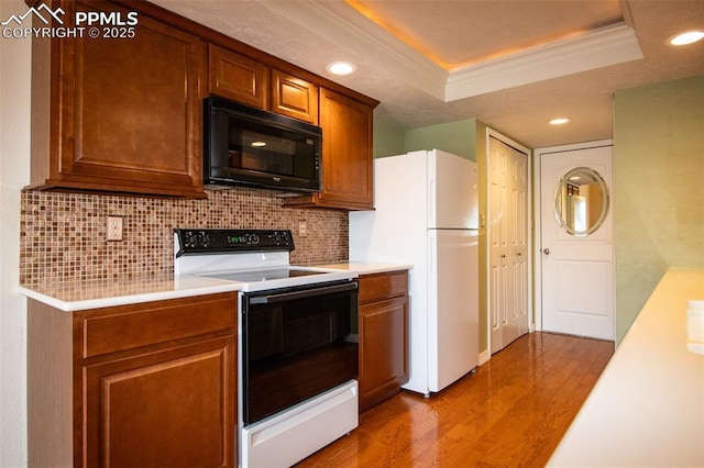 kitchen featuring black microwave, wood finished floors, electric stove, light countertops, and a tray ceiling