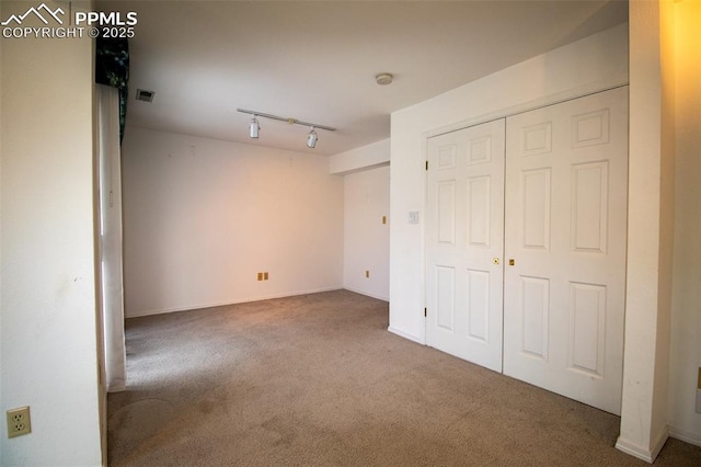 unfurnished bedroom with carpet flooring, visible vents, baseboards, a closet, and track lighting