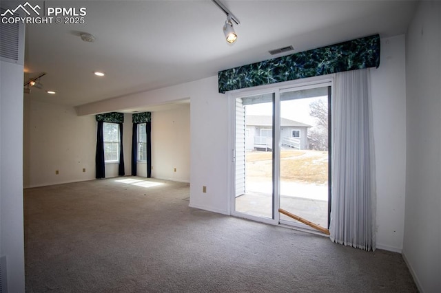 unfurnished room with carpet, baseboards, visible vents, and track lighting