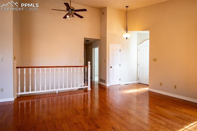 empty room with baseboards, visible vents, ceiling fan, wood finished floors, and a high ceiling