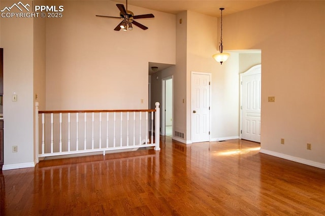 empty room with visible vents, a high ceiling, a ceiling fan, wood finished floors, and baseboards