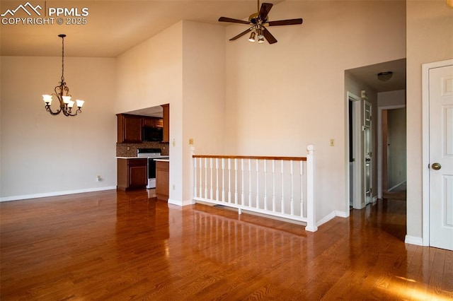 spare room featuring a towering ceiling, dark wood-style floors, baseboards, and ceiling fan with notable chandelier