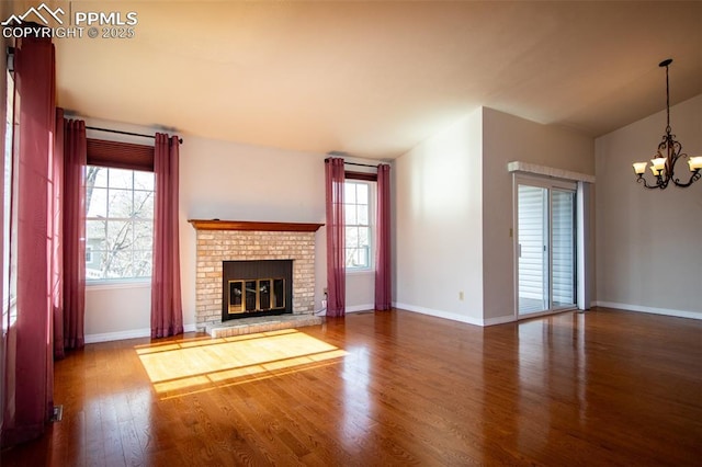 unfurnished living room featuring baseboards, wood finished floors, an inviting chandelier, vaulted ceiling, and a brick fireplace