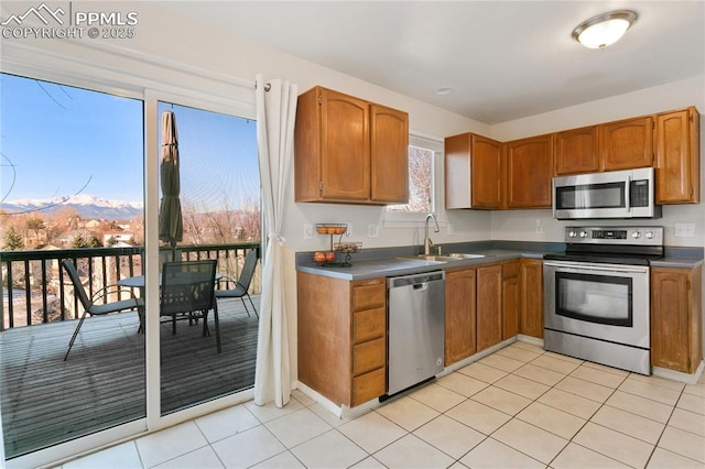 kitchen featuring brown cabinets, stainless steel appliances, a sink, and light tile patterned flooring