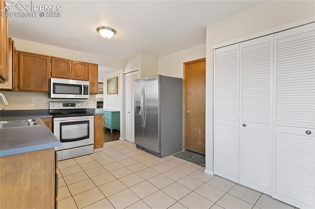 kitchen with light tile patterned floors, stainless steel appliances, a sink, and brown cabinets