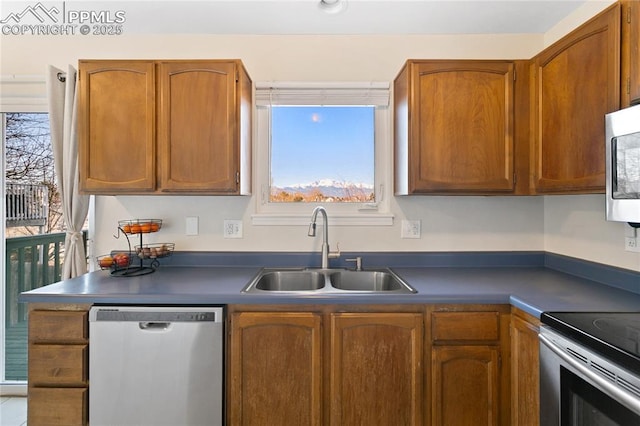 kitchen featuring stainless steel appliances, brown cabinetry, dark countertops, and a sink