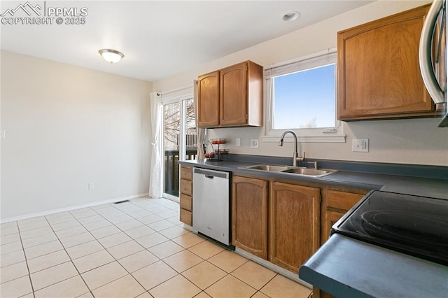 kitchen featuring dark countertops, brown cabinetry, light tile patterned flooring, a sink, and dishwasher