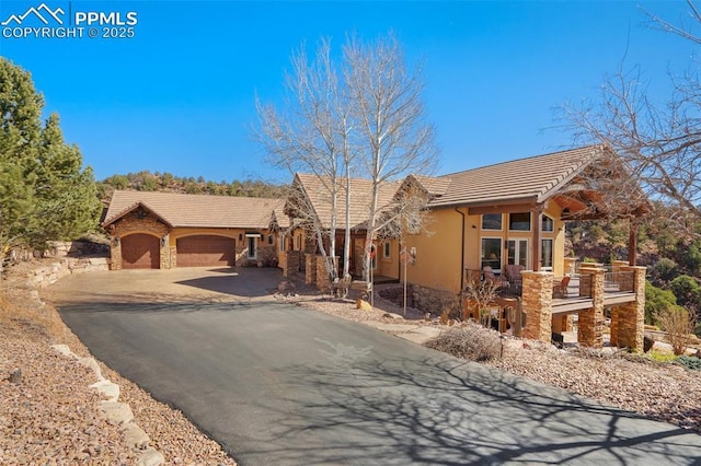 view of front facade featuring driveway, stone siding, a garage, and a tiled roof